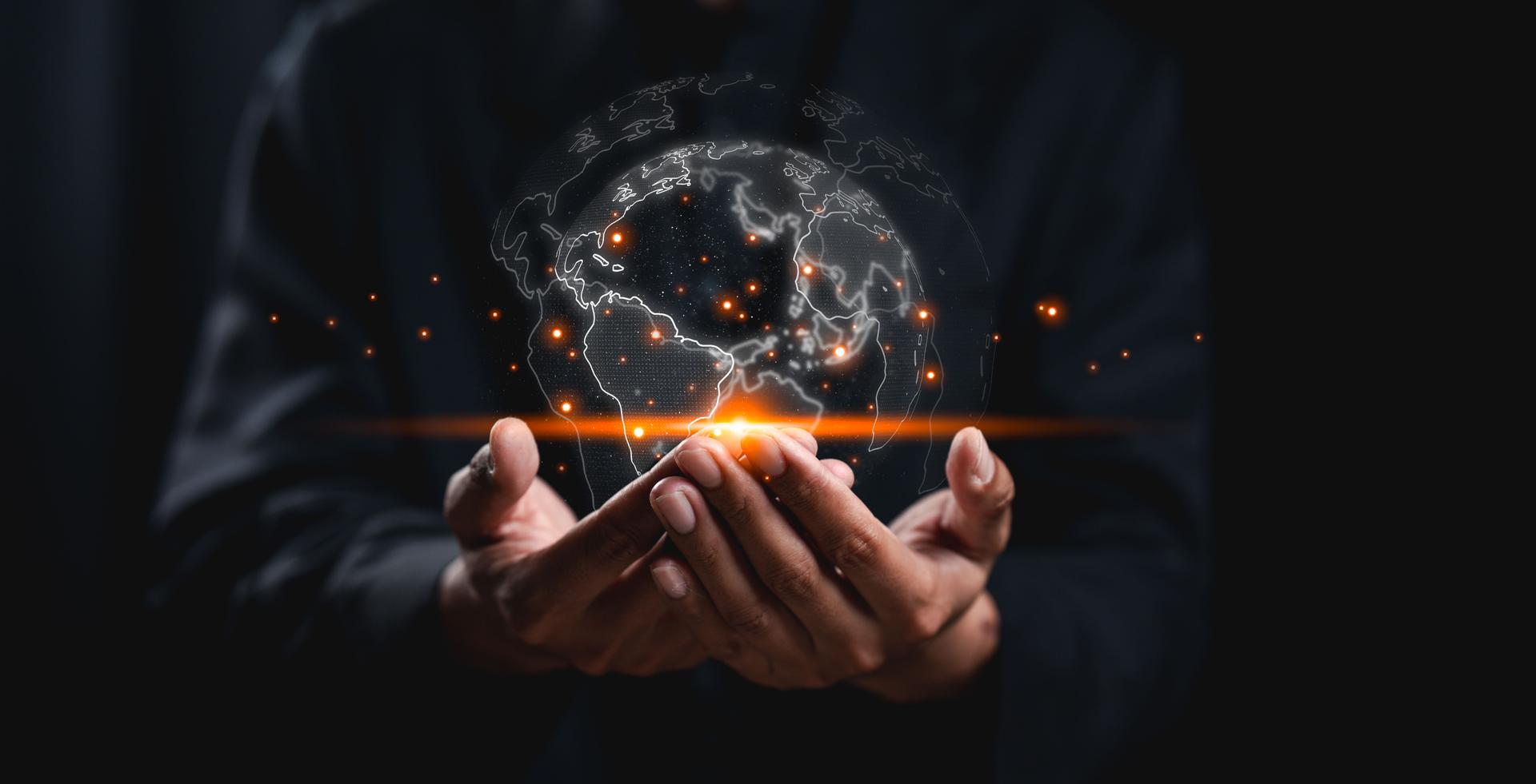 A person holds a glowing, digital globe, surrounded by bright particles, symbolizing global connectivity and innovation against a dark background.